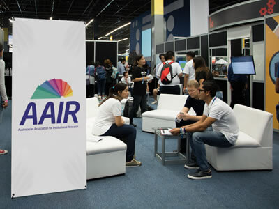 People at a conference with a banner displaying the AAIR logo