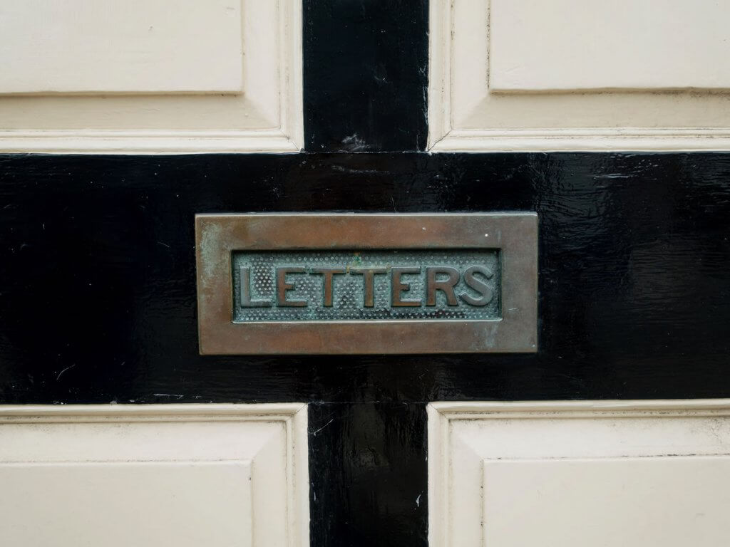 Photo of a letter slot in a door with the words LETTERS written on the slot
