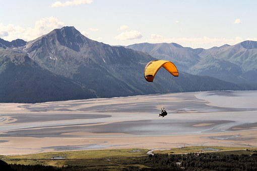 A person parasailing across forests and sands with mountains in the background