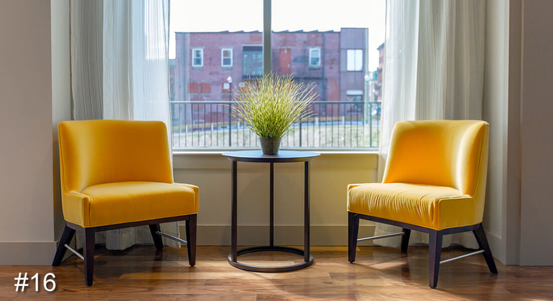 Photo of two yellow chairs and a coffee table in between with a plant on it and a building seen through a window behind