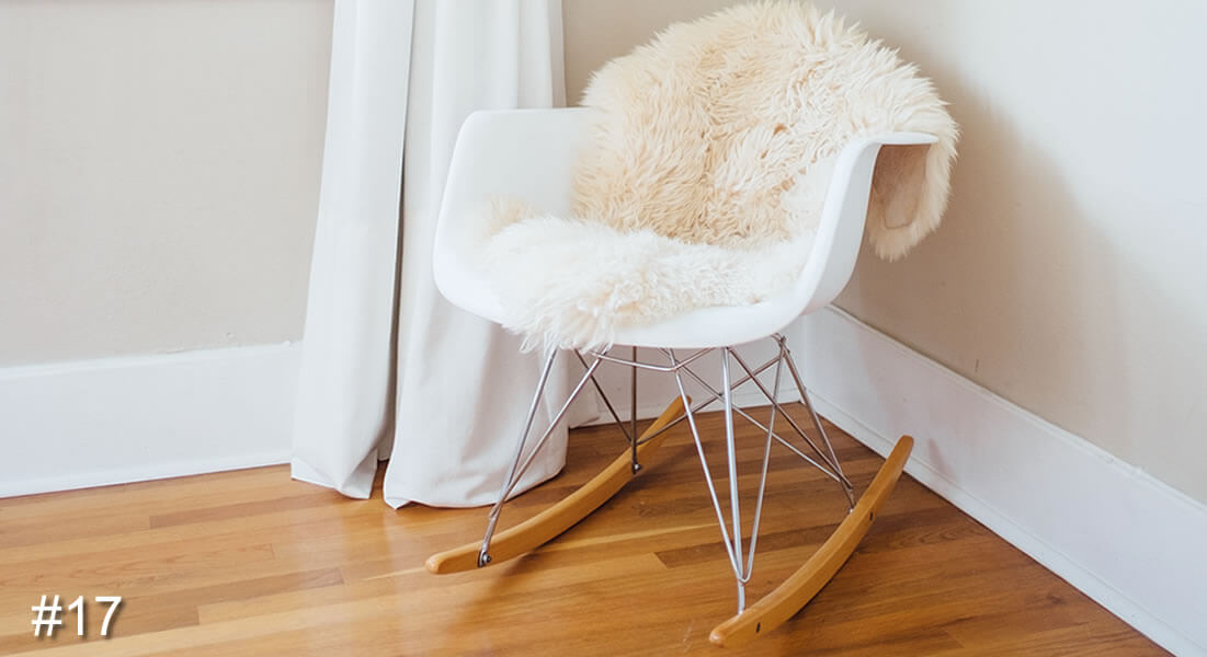 Photo of a small rocking chair with a fluffy rug on it and a curtain behind