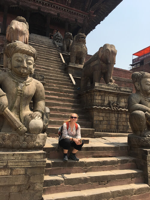 Photo of Liesha Northover sitting next to statues on the steps of an ancient building in Baktapur, Nepal
