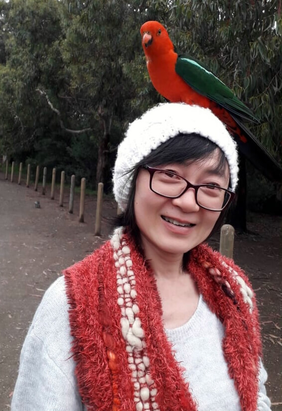 Photo of Lifen Sudirjo wearing a red handmade scarf and glasses with a king parrot on her head