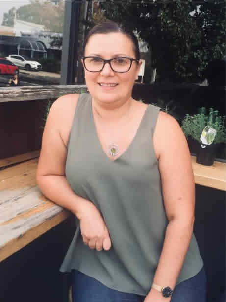 Photo of Julia Petrou wearing glasses and leaning against a bench
