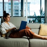 Photo of a woman reclining on the couch in her living room with a laptop on her knee.