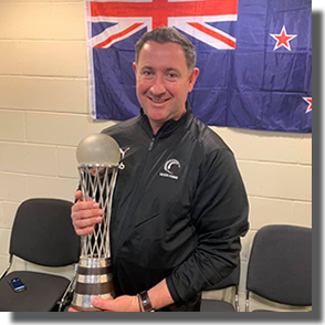 Photo of Hayden Croft holding a trophy with the NZ flag behind him.