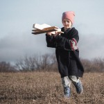 Photo of a young girl running in a field with a wooden airplane
