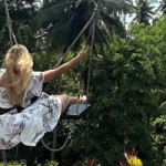 Photo of Alex on a swing out in nature, with a white dress flowing behind.