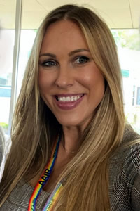 Photo of Alex Sieniarski smiling with long blonde hair wearing an AAIR rainbow lanyard.