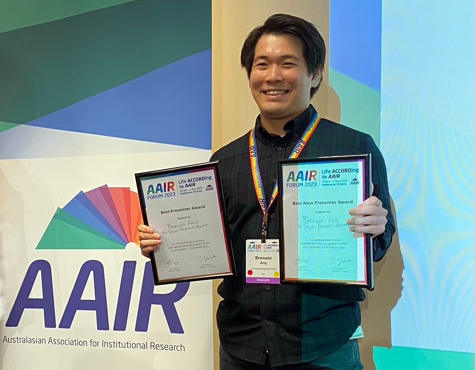 Brenwin Ang holding up his two certificates: Best Presenter and best New Presenter Awards. The AAIR pullup banner is in the background.