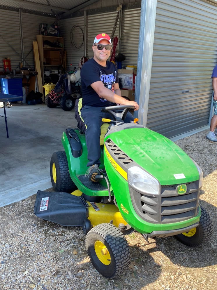 Photo of a man driving a ride-on lawnmower out of a shed.