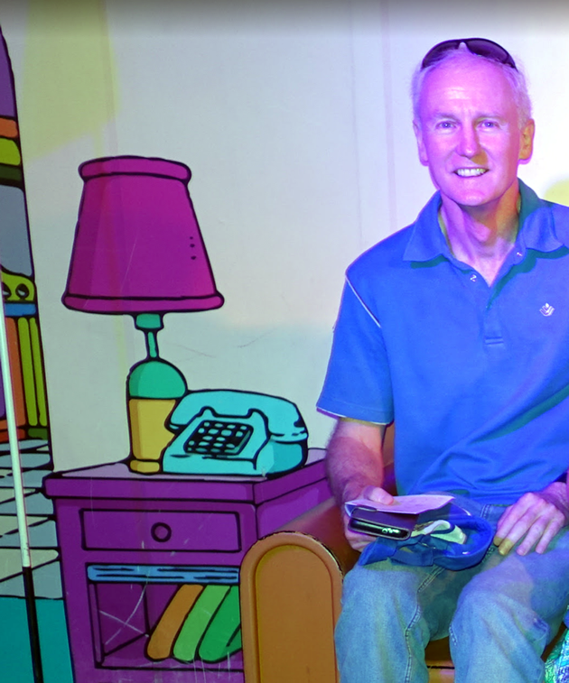 Photo of Peter Hayes sitting in The Simpsons chair. The chair is real, but the surroundings are in cartoon format and look exactly like Homer Simpson's living room.